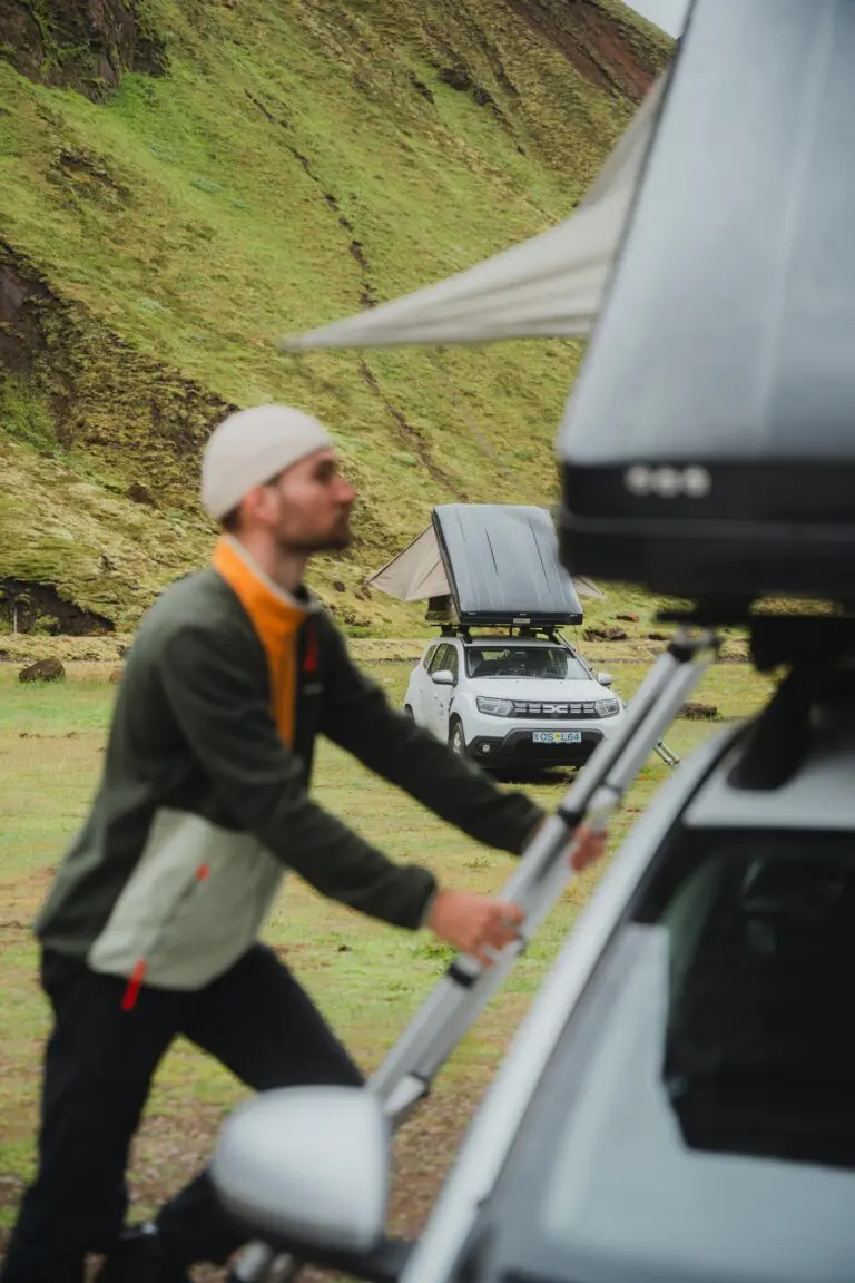 man setting up a rooftop tent on a car in a green landscape
