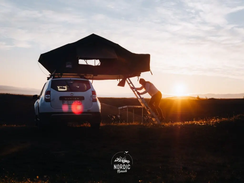 person climbing into rooftop tent on car at sunset
