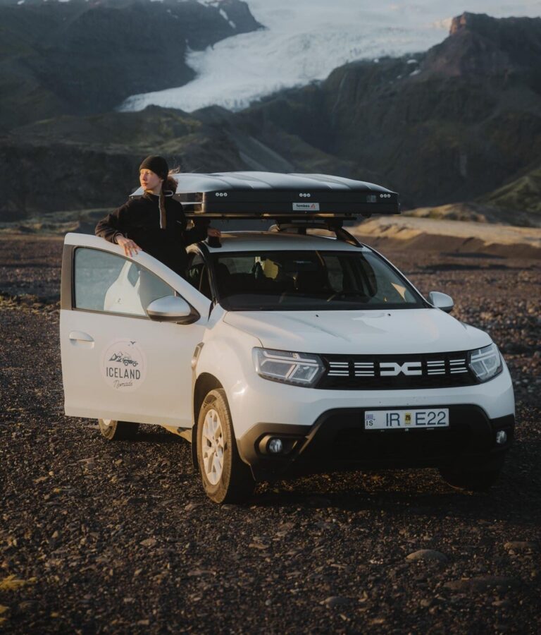 person standing by car with rooftop tent in front of glacier