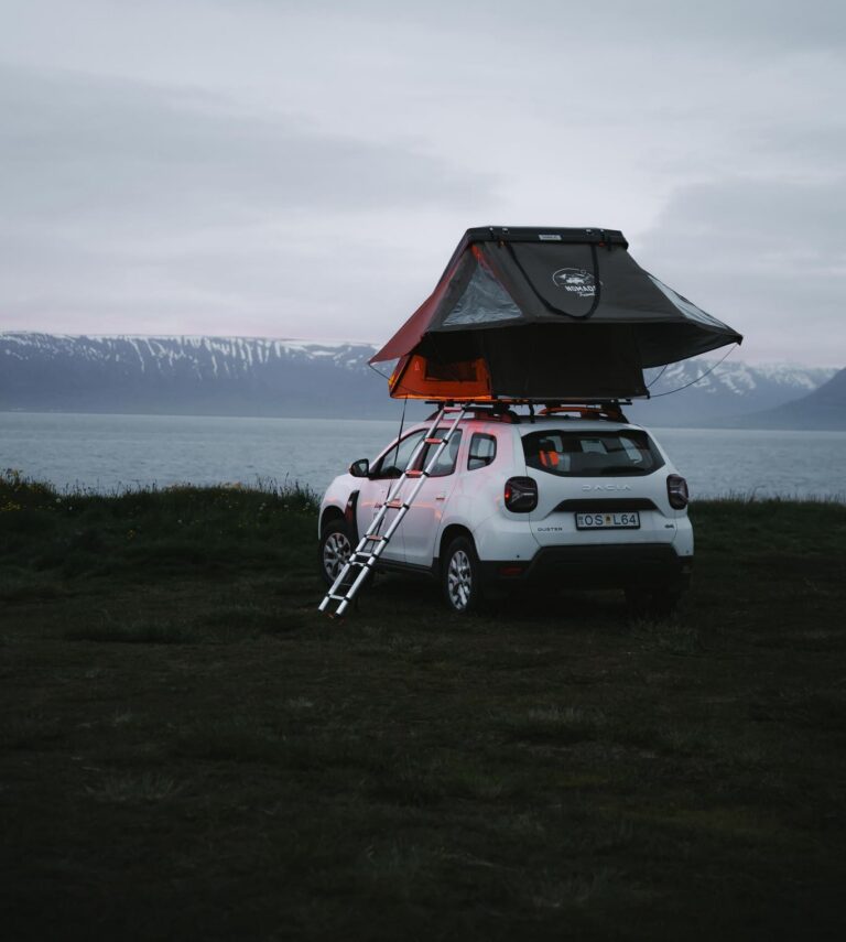 white car with rooftop tent by a lake and mountains