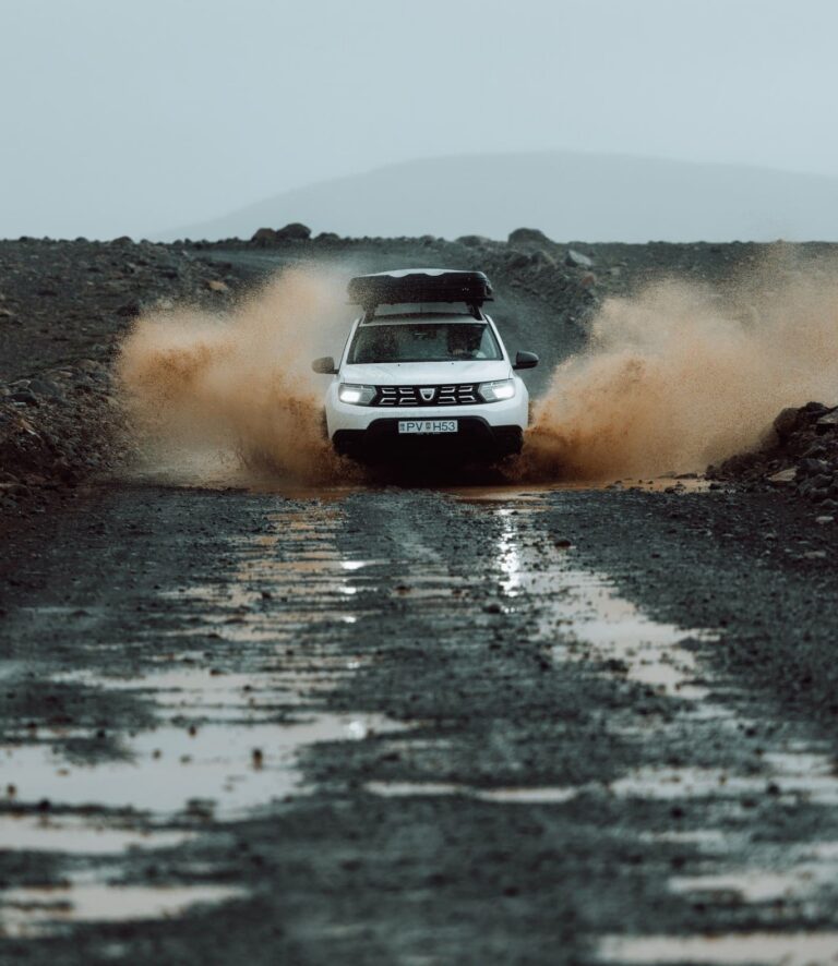 white car splashing through muddy water on a gravel road